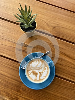 Latte art cappuccino and cactus plant on a wood table