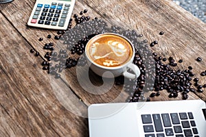Latte art coffee cup and coffee bean with laptop computer on wood background