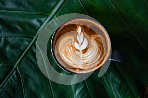 Latte art coffee cup on green leaf background