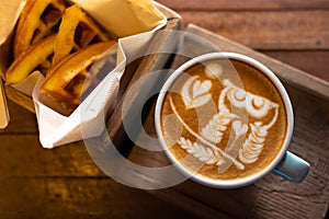 Latte art coffee with waffles on wooden table