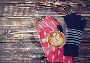 Latte art coffee in a yellow cup with black yarn gloves, and red fabric on the old wooden table background top view, flat lay