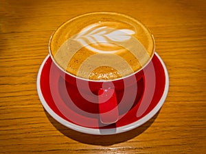 Latte Art. Hot latte coffee on wooden table. Morning with a red cup of cappuccino. Art and craft coffee.
