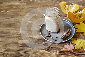 Latte coffee cacao with milk, pumpkin, cinnamon spice in glass transparent cup, mug, on wooden background, hot warm autumn