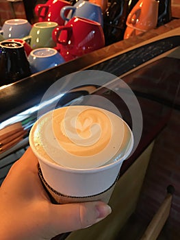 Latte coffee, cappuccino in a disposable paper cup with the image of a flower - a heart against the background of bright multicolo