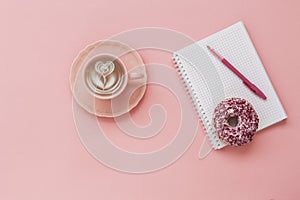 Latte Coffee cup, delicious pink donut with sprinkle, notebook for notes and pen on pink paper background