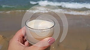 Latte coffee in female hand against sea waters