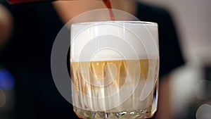 Latte in glass. close-up, barista makes latte, gently adds coffee to frothed milk, in a beautiful glass.