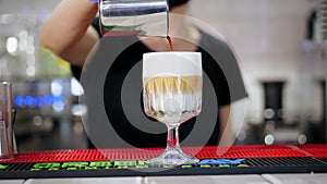 Latte in glass. close-up, barista makes latte, gently adds coffee to frothed milk, in a beautiful glass.