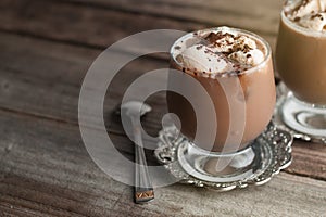 Latte macchiato in a glass with cream on wooden background, decorated withcocoa powder and cinnamon, vintage style. Copy space.