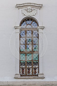Lattices on a narrow long window in the white wall of the temple. Exterior. Vertical photo