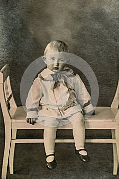 Latvia - CIRCA 1920-1925: A portrait of child sitting on wave bench in studio, Vintage Carte de Viste Art Deco era photo