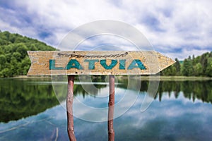 Latvia wooden arrow road sign against lake and forest background. Travel to Latvia concept