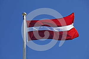 Latvian flag waving in the wind on a blue summer sky