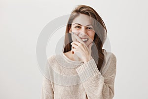 Laugh increases life span. Studio shot of positive young woman with brown hair chuckling and covering mouth with hand