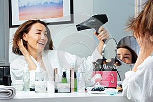 Laughing adult woman in housecoat holding hairdryer dry hair photo