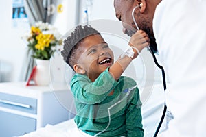 Laughing african american boy patient taking male doctor's stethoscope in hospital