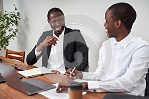 Laughing African American businessmen discussing paperwork with a coworker at a table in an office