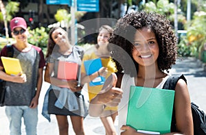 Laughing african american female student showing thumb with group of international students