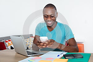 Laughing african american man sending message with phone at home