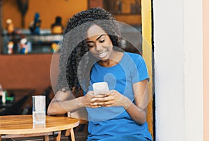 Laughing african american woman at bar texting message with mobile phone