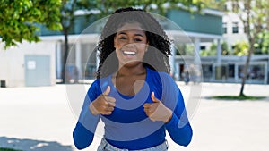 Laughing african american young adult woman showing thumbs up in the city