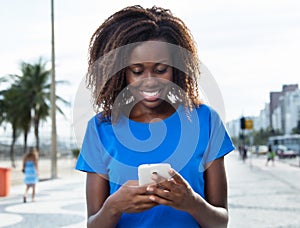 Laughing african woman in a blue shirt sending message with phone