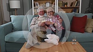 Laughing aged couple, man and woman watching tv, comedy show or movie and eating popcorn snack, sitting on cozy couch at home,