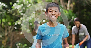 Laughing asian boy wearing volunteer t shirt holding refuse sack for collecting plastic waste