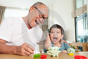 Laughing Asian Grandfather and Grandson making toys from plasticine