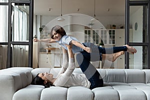 Laughing Asian mother lying on couch, lifting 7s son