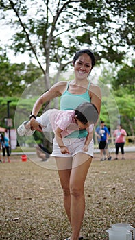 Laughing Asian woman carrying toddler and participating in family games outdoor