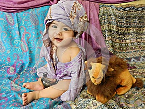 Laughing baby boy dressing in turban sits on Asian fabrics