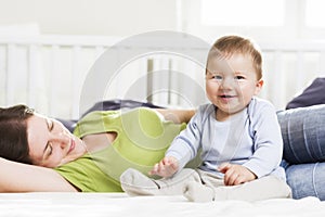 Laughing baby boy sitting in bed together with his mother.