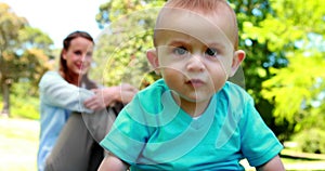 Laughing baby boy sitting on the grass with mother behind him