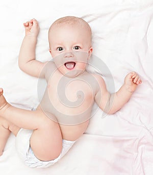 Laughing baby in diaper laying on the white bed
