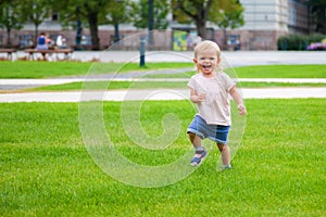 Laughing baby girl running on the green grass