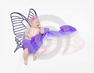 Laughing baby girl wrapped in fabric on cloud with painted butterfly wings