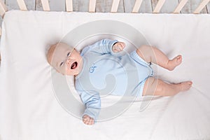 laughing baby lies in the crib  cute little boy of six months lies in the nursery on the bed and laughs