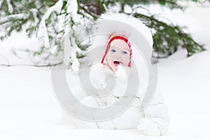 Laughing baby sitting in snow under a Christmas tree