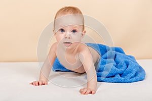 Laughing baby wearing diaper and blue towel on bed after bath, shower