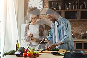 Laughing black couple preparing salad in kitchen