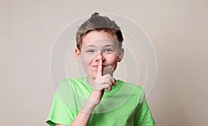 Laughing boy doing a silence gesture. Kid putting finger up to l
