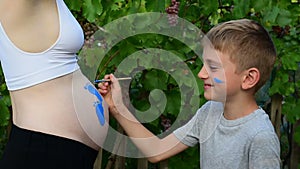 Laughing boy draws with a brush on the belly of his pregnant mom baby`s footprint. Pregnant concept. Close-up