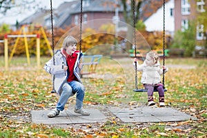 Laughing boy and his toddler sister on a swing