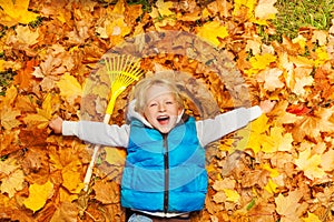 Laughing boy laying on the autumn leaves with rake