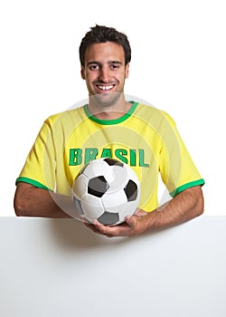 Laughing brazilian soccer fan with ball behind signboard