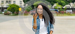 Laughing brazilian young adult woman using a smart phone voice recognition