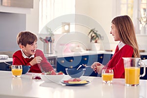 Laughing Brother And Sister Wearing School Uniform In Kitchen Having Fun As They Eat Healthy Breakfast
