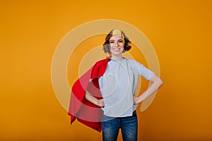 Laughing brunette girl in superhero outfit posing on yellow background. Joyful lady enjoying masquerade and posing in