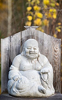 The Laughing Buddha, Budai, with his cloth sack stone sculpture with yellow fall colors in the background photo